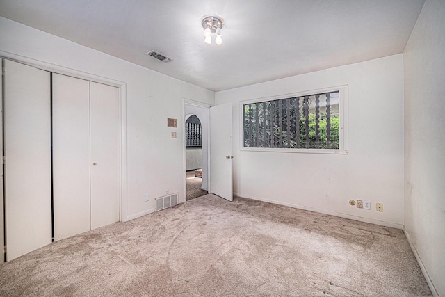 unfurnished bedroom featuring carpet floors, arched walkways, a closet, and visible vents