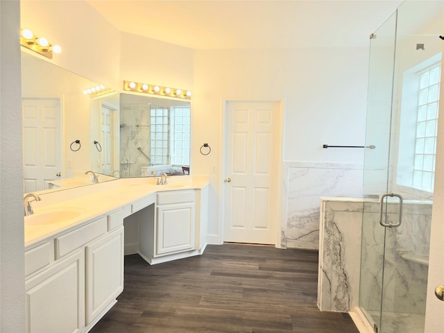 full bath with a sink, a marble finish shower, double vanity, and wood finished floors