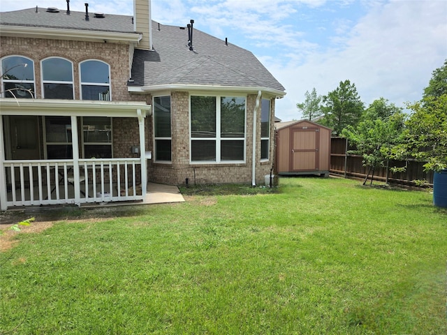 back of property featuring roof with shingles, brick siding, a storage shed, a fenced backyard, and a yard
