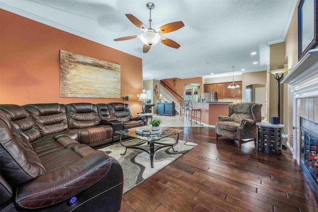 living area featuring crown molding, a ceiling fan, a tiled fireplace, and hardwood / wood-style flooring
