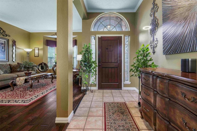 foyer entrance featuring a textured ceiling, light tile patterned floors, baseboards, ornamental molding, and a textured wall