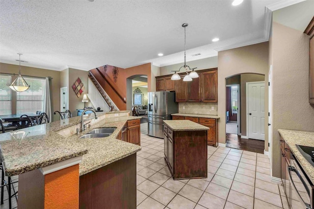 kitchen featuring ornamental molding, stainless steel fridge, arched walkways, a large island with sink, and a sink