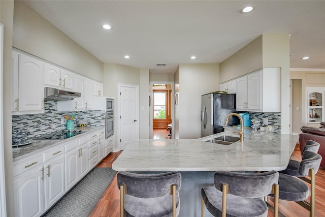 kitchen with appliances with stainless steel finishes, wood finished floors, a sink, a peninsula, and under cabinet range hood