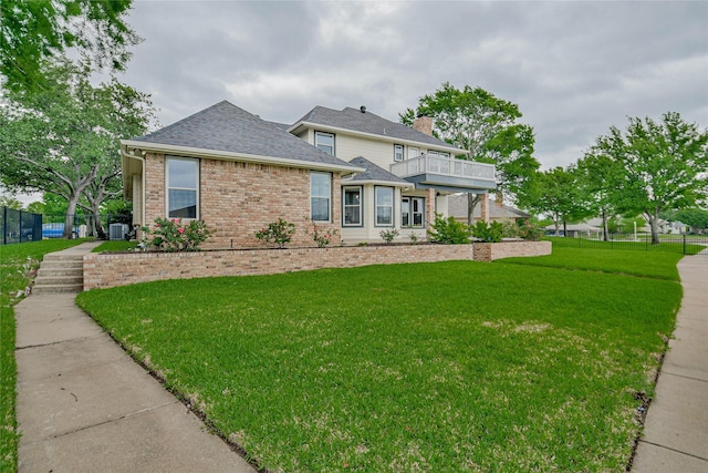 traditional home featuring fence, brick siding, a front yard, a chimney, and a balcony