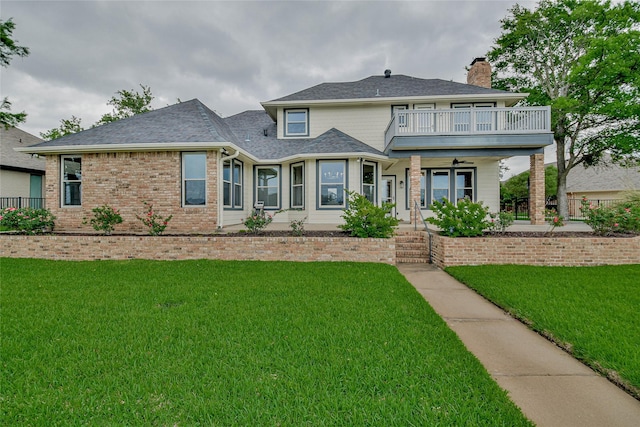 view of front of house with a chimney, a front yard, ceiling fan, and a balcony