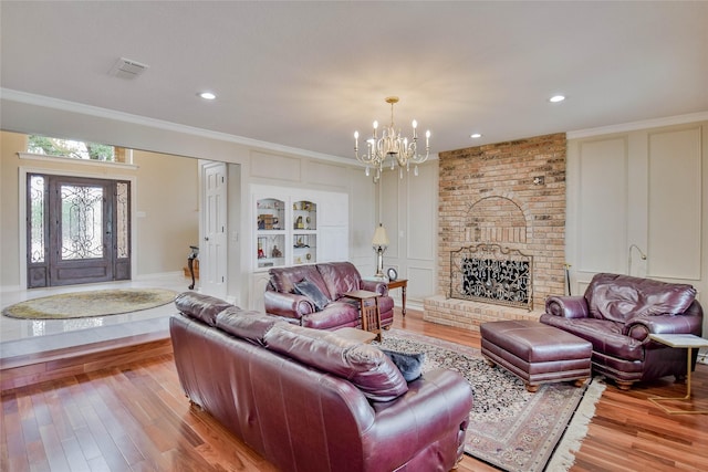 living area featuring visible vents, ornamental molding, a brick fireplace, light wood-type flooring, and a notable chandelier