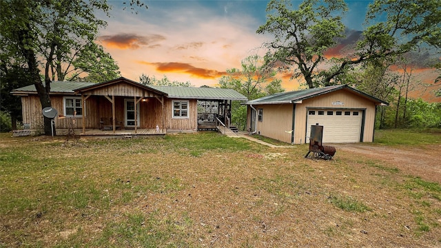 view of front of house featuring covered porch, driveway, metal roof, a front yard, and a detached garage