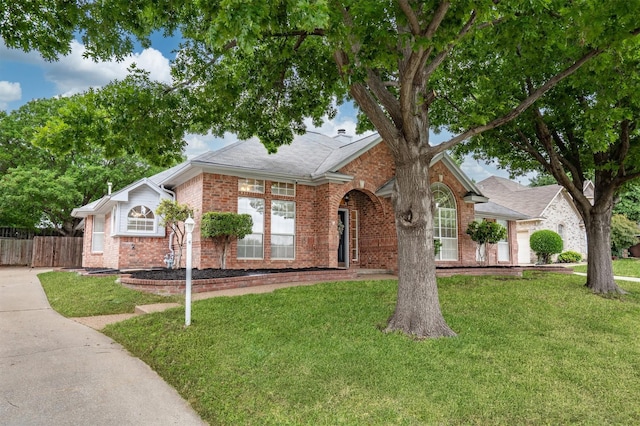 single story home featuring fence, a shingled roof, a front yard, and brick siding