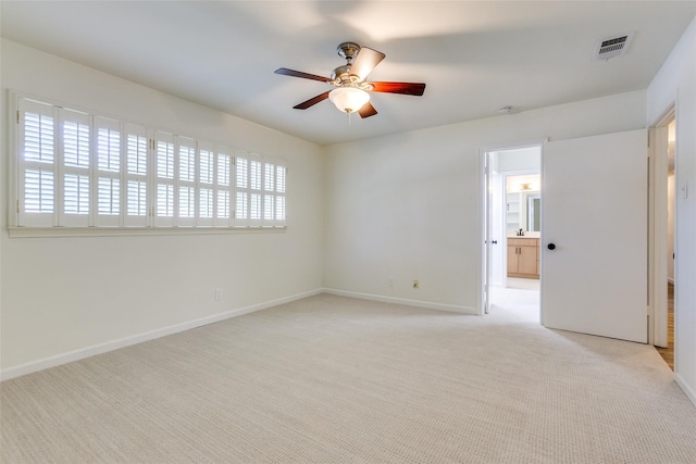 spare room featuring light colored carpet, ceiling fan, visible vents, and baseboards