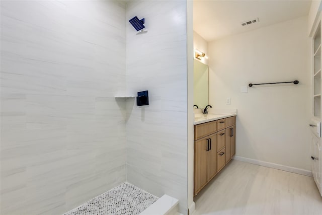 bathroom with vanity, baseboards, a tile shower, and visible vents