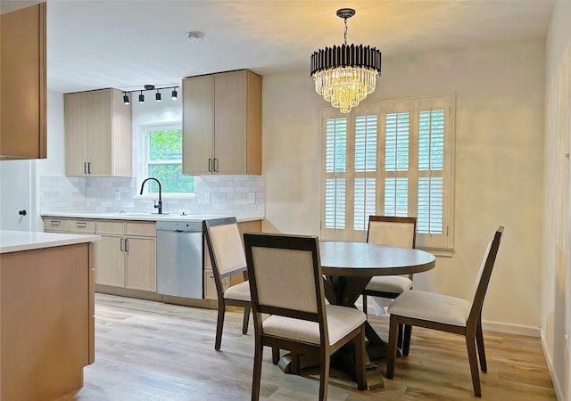 kitchen featuring decorative backsplash, stainless steel dishwasher, a sink, light countertops, and light wood-style flooring