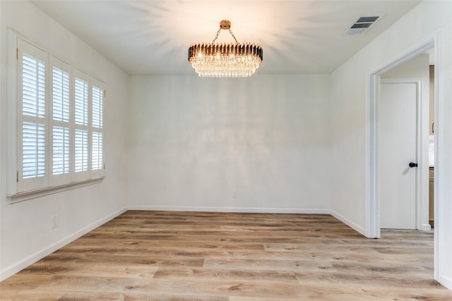 unfurnished room with visible vents, light wood-style flooring, baseboards, and a chandelier