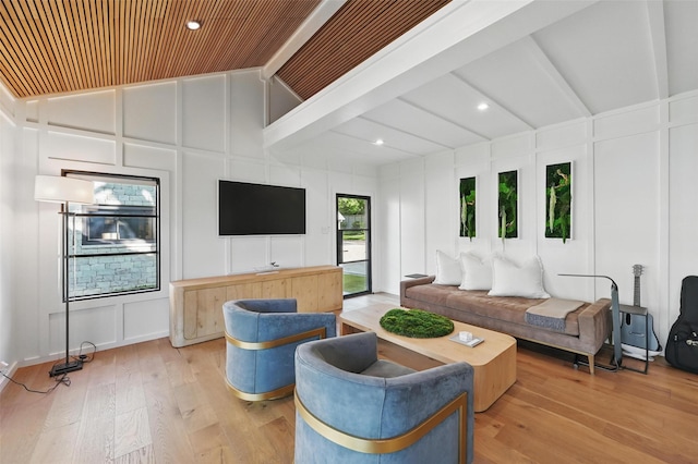 living area featuring vaulted ceiling with beams, wood finished floors, and a decorative wall
