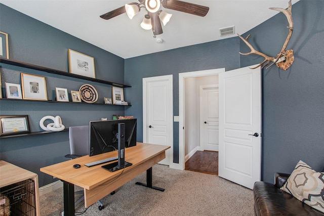 office space with carpet flooring, ceiling fan, a textured wall, baseboards, and visible vents