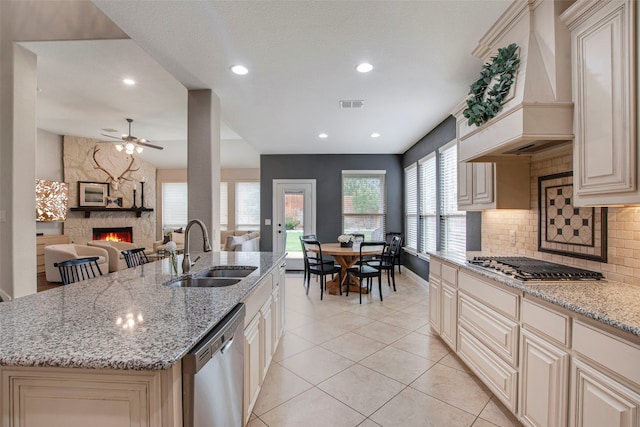 kitchen featuring a stone fireplace, appliances with stainless steel finishes, cream cabinets, a sink, and custom range hood