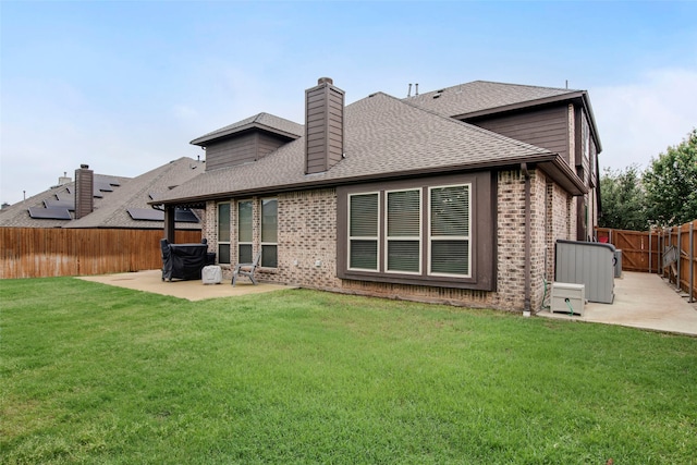 back of house featuring a chimney, roof with shingles, a lawn, a fenced backyard, and a patio