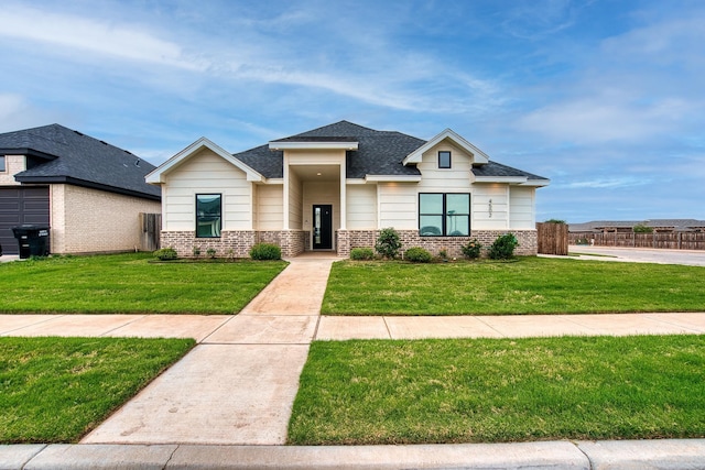 view of front of house with a shingled roof, a front yard, and brick siding