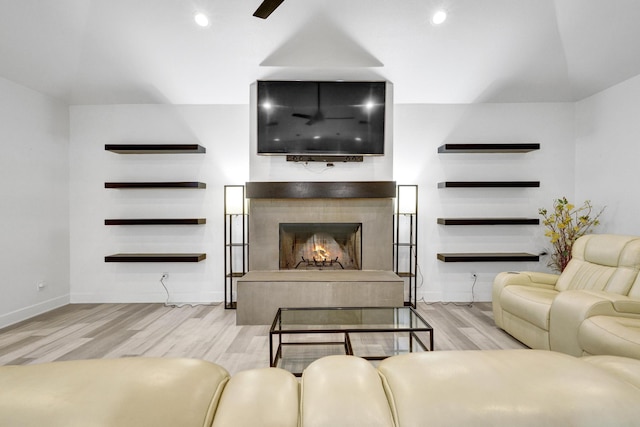 living room featuring a warm lit fireplace, recessed lighting, baseboards, and wood finished floors