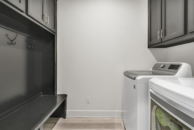 clothes washing area with light wood-type flooring, cabinet space, baseboards, and washing machine and clothes dryer