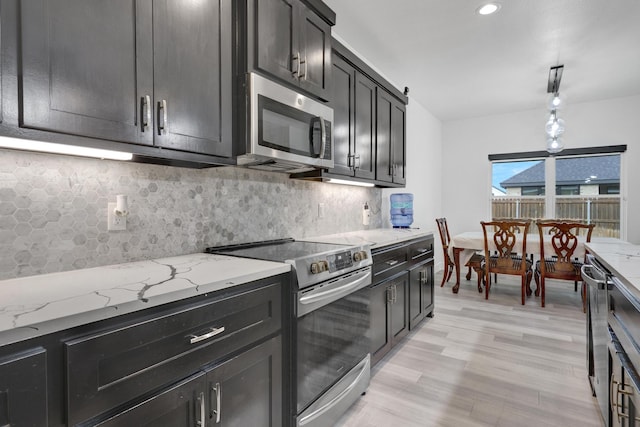 kitchen with appliances with stainless steel finishes, decorative backsplash, light stone countertops, and light wood-style flooring