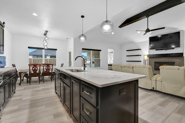 kitchen with a sink, a lit fireplace, light wood-style flooring, and decorative light fixtures