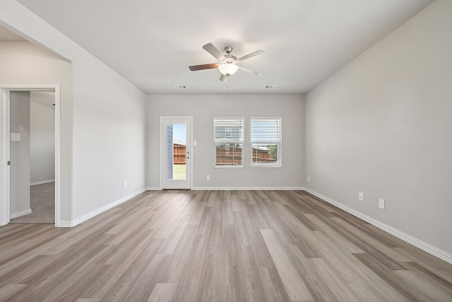 empty room with light wood-type flooring, a ceiling fan, baseboards, and visible vents