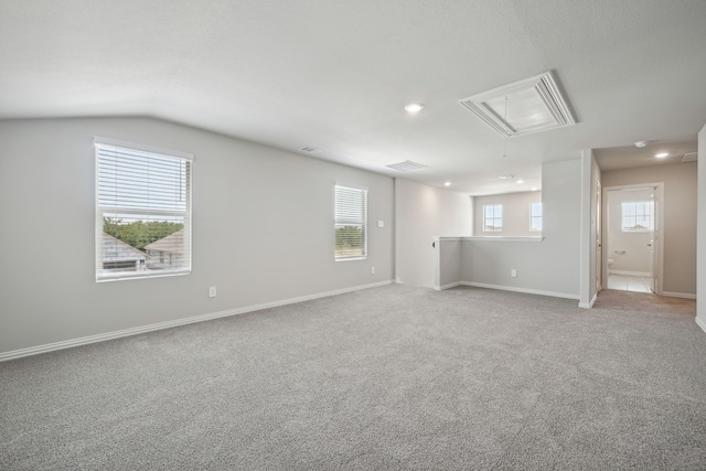 empty room featuring baseboards, lofted ceiling, light carpet, and attic access