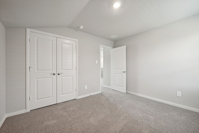 unfurnished bedroom featuring carpet flooring, baseboards, lofted ceiling, visible vents, and a closet