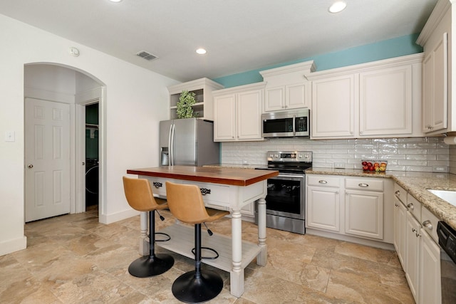 kitchen featuring stone finish floor, tasteful backsplash, stainless steel appliances, and visible vents