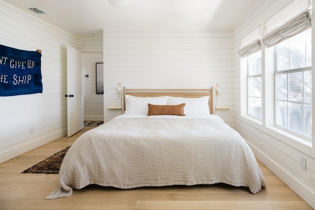 bedroom with visible vents, wood walls, and wood finished floors