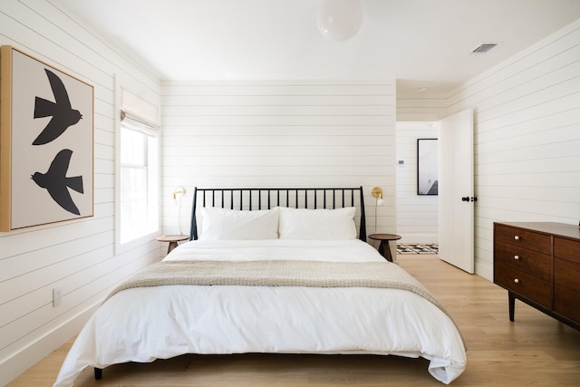bedroom featuring light wood finished floors, wood walls, and visible vents