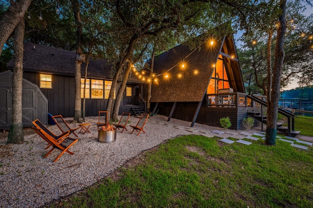 back of property featuring stairway, a storage shed, roof with shingles, and an outdoor fire pit