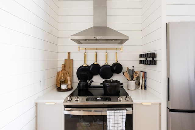 kitchen featuring light countertops, appliances with stainless steel finishes, wood walls, and wall chimney exhaust hood