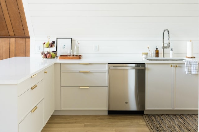 kitchen with stainless steel dishwasher, a sink, light countertops, light wood finished floors, and a peninsula