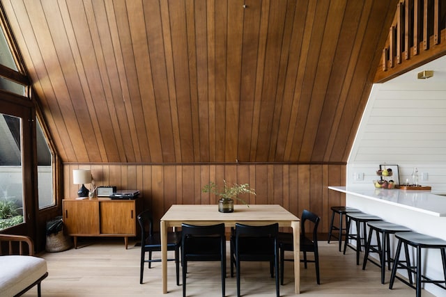 dining area featuring wooden walls, vaulted ceiling, and light wood-style floors