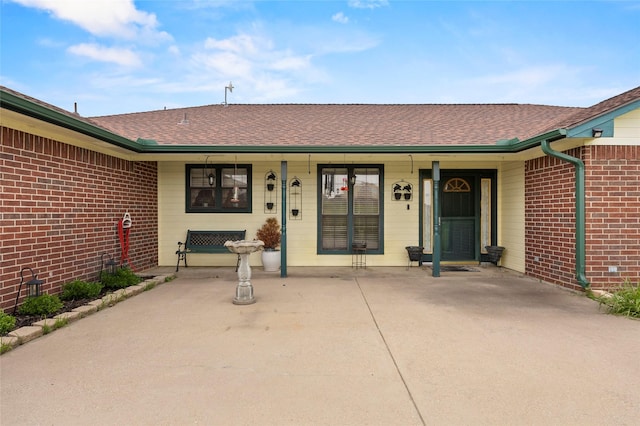 property entrance featuring a porch, a shingled roof, and brick siding
