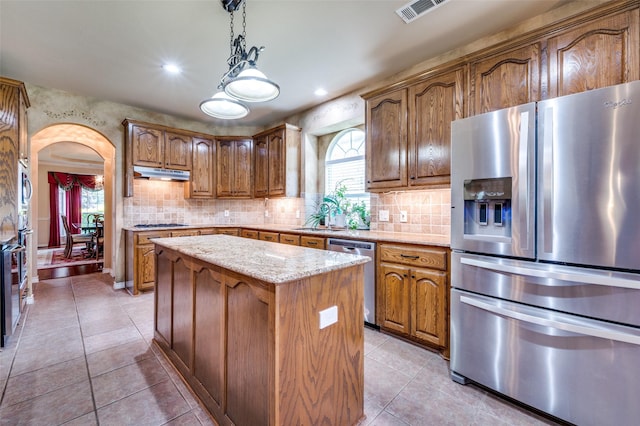 kitchen with stainless steel appliances, decorative backsplash, under cabinet range hood, visible vents, and a kitchen island