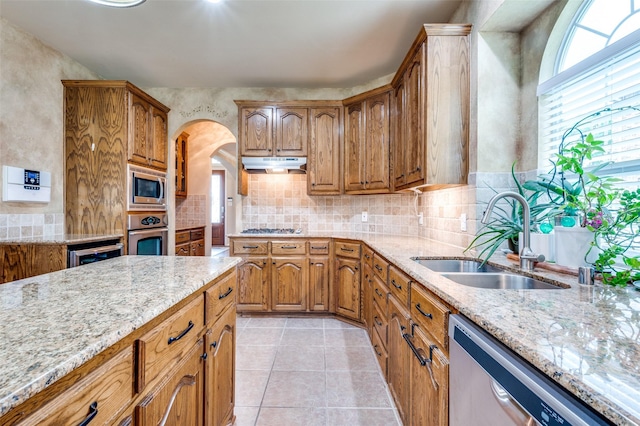 kitchen with a sink, stainless steel appliances, under cabinet range hood, and light stone counters