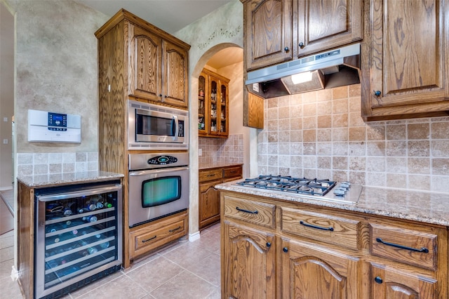 kitchen with light stone counters, beverage cooler, backsplash, stainless steel appliances, and under cabinet range hood