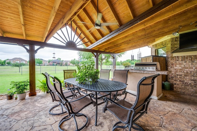 view of patio featuring fence, an outdoor kitchen, a ceiling fan, a gazebo, and outdoor dining space