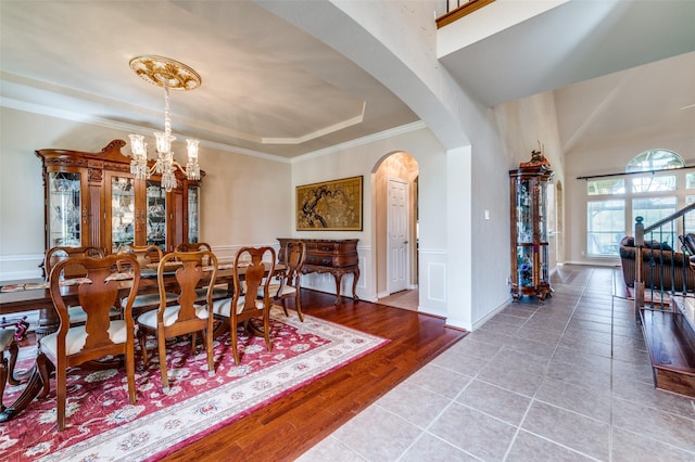 tiled dining area with ornamental molding, wainscoting, a tray ceiling, a chandelier, and arched walkways