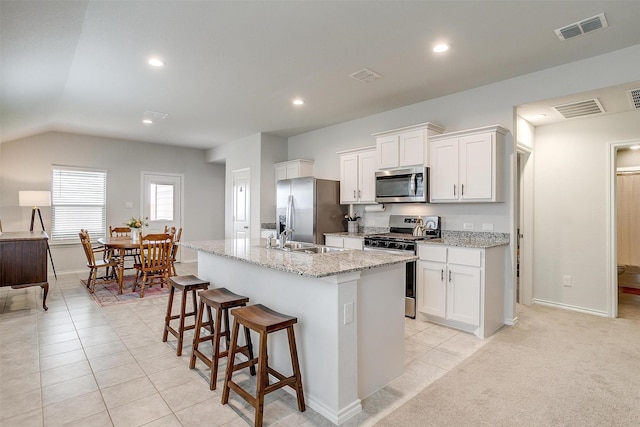 kitchen featuring white cabinets, stainless steel appliances, visible vents, and a center island with sink