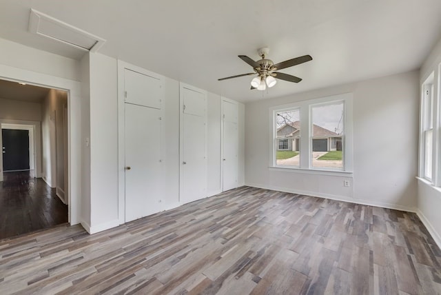 unfurnished bedroom featuring baseboards, ceiling fan, attic access, and wood finished floors