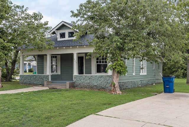 view of front of house featuring a porch, a shingled roof, a front lawn, and stone siding