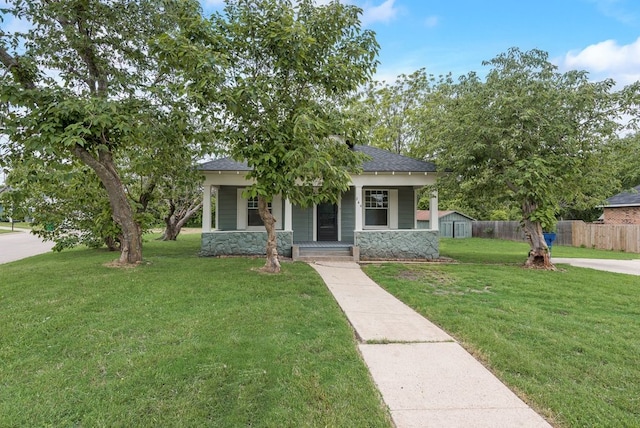 view of front of house featuring a front lawn, fence, covered porch, stone siding, and roof with shingles