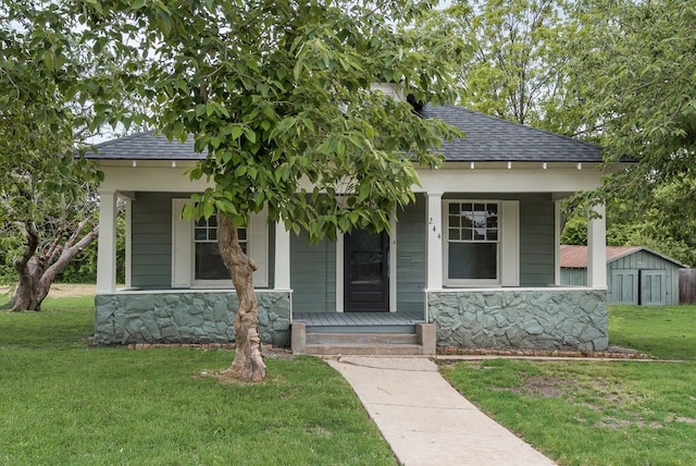 view of front of house featuring covered porch, a shingled roof, a front lawn, and stone siding