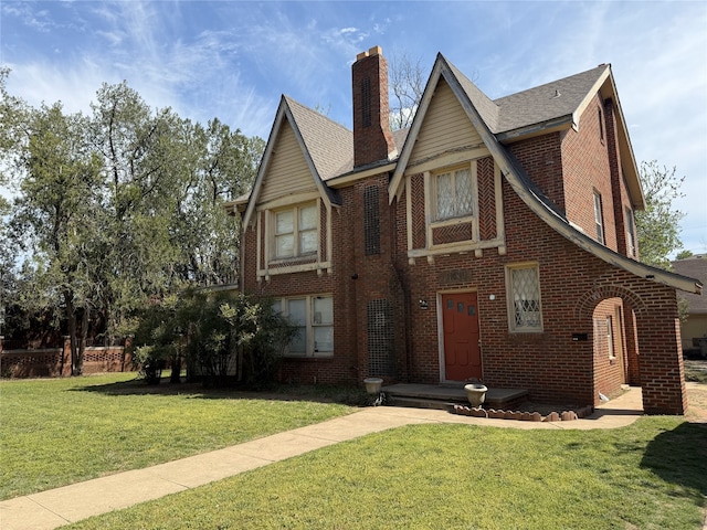 english style home featuring a chimney, a front lawn, and brick siding