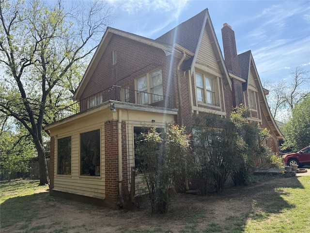 view of side of home with a chimney, brick siding, and a balcony