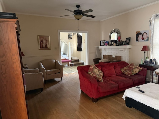 living area with crown molding, a brick fireplace, wood finished floors, stairway, and a ceiling fan