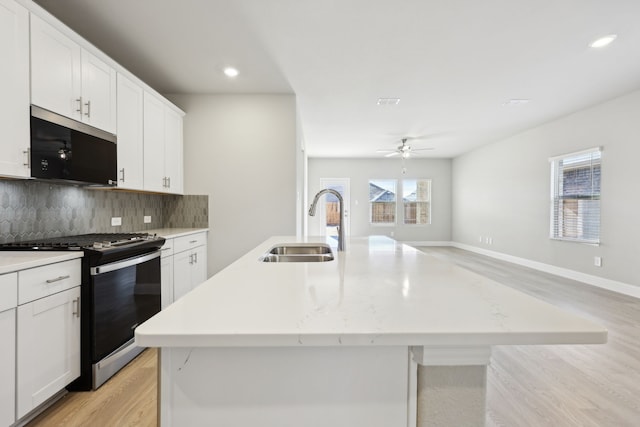 kitchen featuring a center island with sink, recessed lighting, a sink, backsplash, and gas stove